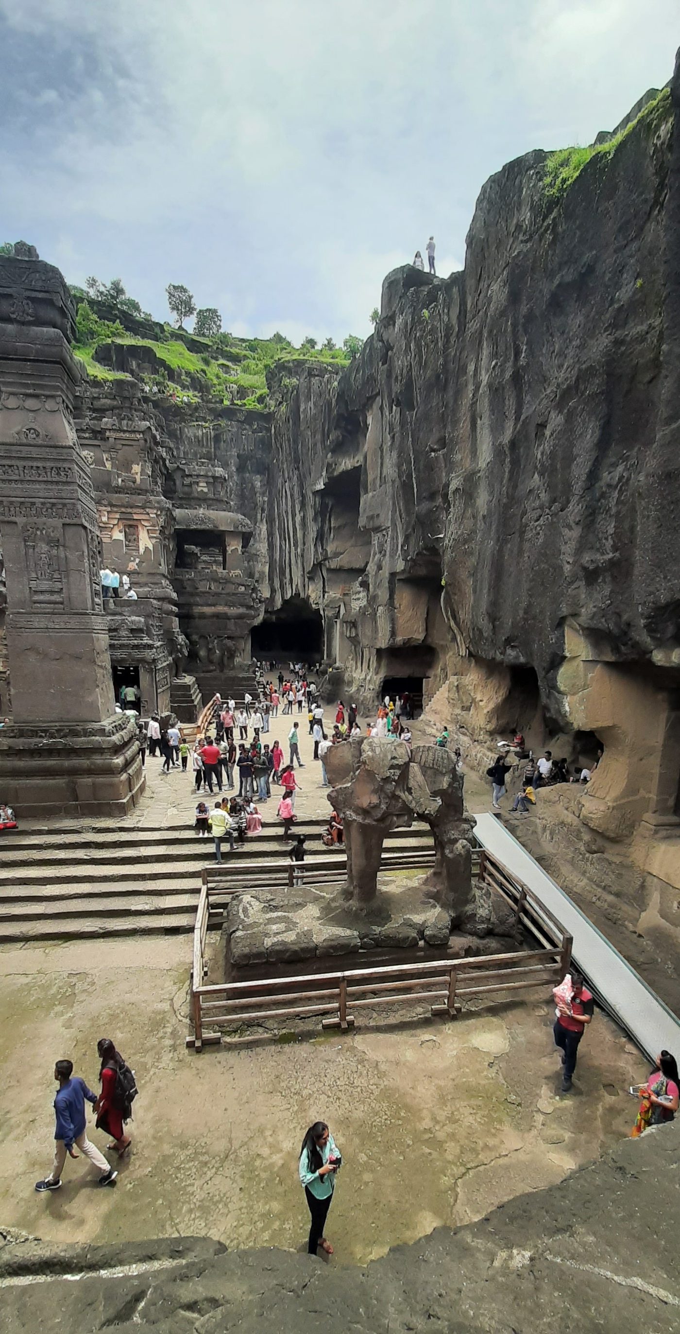 The Kailasa courtyard from the rim — the subtracted mountain, with a stone elephant on guard and visitors for scale.